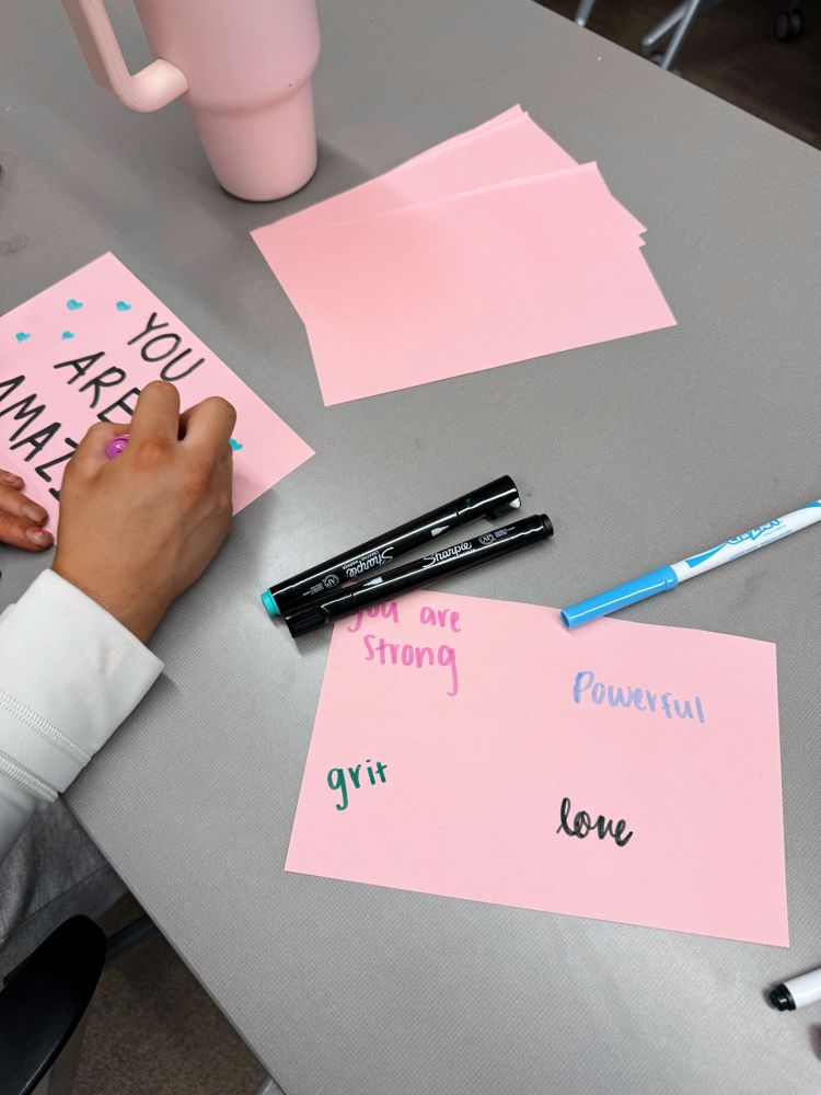 Pink cards being written with the words strong, powerful, grit and love