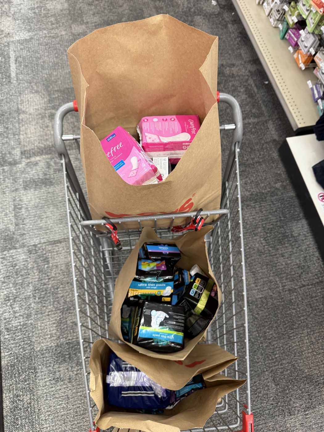 A shopping cart with paper bags full of pads and period products